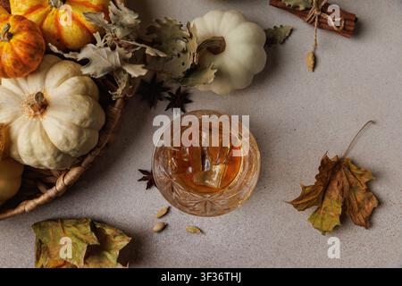 Oberansicht von Whiskey mit Eiswürfeln neben weißen Kürbissen, Gewürzen und getrockneten Blättern auf einer strukturierten Oberfläche.. Stockfoto
