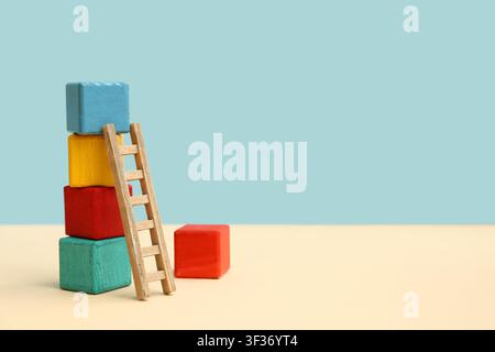 Bunte Bauwürfel mit Holzleiter auf farbigem Hintergrund Stockfoto