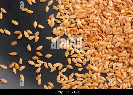 Rohe goldene Leinsamenkörner (Leinsamen) verstreut auf einer dunklen schwarzen Oberfläche. Gesundes organisches Superfood reich an Omega-3 und Ballaststoffen Stockfoto
