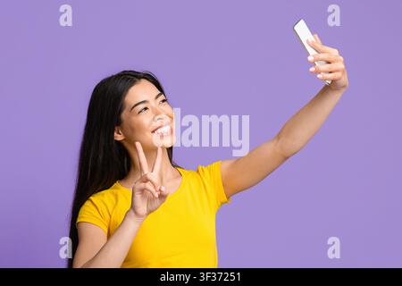 Selfie-Spaß. Fröhliche Asiatische Frau, Die Selbstporträt Auf Smartphone, Zeigt Frieden Geste Stockfoto