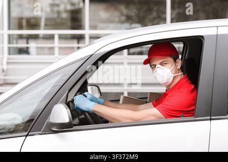 Lieferung Mann in roter Uniform in medizinischen Maske und Handschuhe Auto fahren Stockfoto