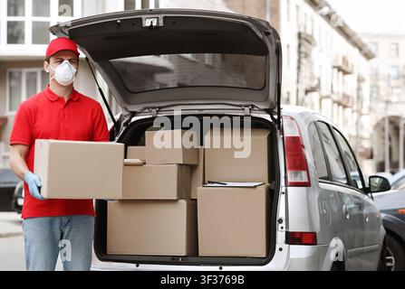 Viele Aufträge, viele Lieferkonzepte. Kurier hält großes Paket in der Nähe des Autos Stockfoto