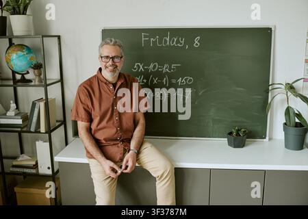 Porträt eines mittelalten männlichen Lehrers, der an einer Tafel sitzt Stockfoto