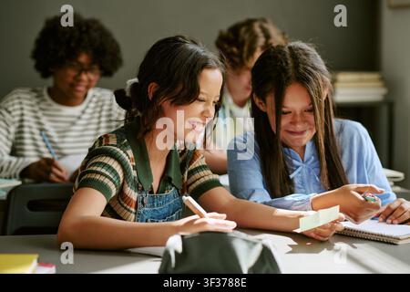 Verschiedene Teenager-Mädchen lächeln, während sie während der Hausaufgaben Notizen lesen Stockfoto