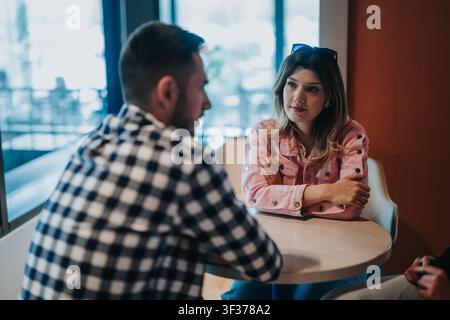 Junge Frau und Mann führen ein ernstes Gespräch an einem Cafétisch während des Tages Stockfoto