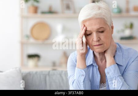 Ältere Frau, Die Zu Hause Kopfschmerzen Hat Und Sich Unwohl Fühlt Stockfoto