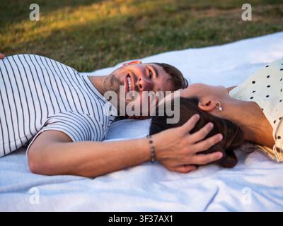 Ein junges Paar entspannt sich auf einer weichen Picknickdecke in einem sonnigen Park und genießt die gemeinsame Gesellschaft. Stockfoto