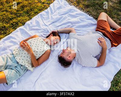 Ein lächelndes Paar genießt einen ruhigen Moment auf einer Picknickdecke während eines sonnigen Nachmittags im Park. Stockfoto