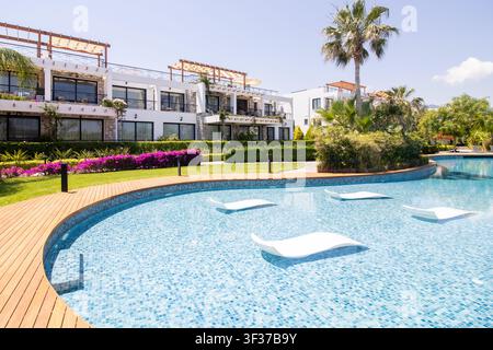 Luxus-Ferienwohnungen mit einem geschwungenen Schwimmbecken, das über im Wasser liegende Loungesessel verfügt, in einer landschaftlich gestalteten Resort-Umgebung an einem sonnigen Tag Stockfoto
