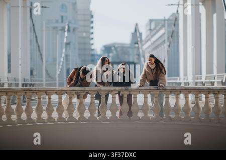 Freunde lachen und haben Spaß auf einer Stadtbrücke im Winter und tragen Mäntel und Sonnenbrillen Stockfoto