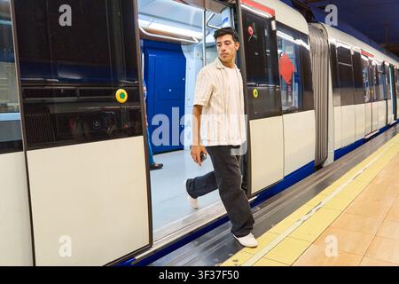 Junger Mann in lässiger Kleidung, der aus einem Metrozug auf den Bahnsteig in einer U-Bahn-Station in Madrid, Spanien, steigt Stockfoto