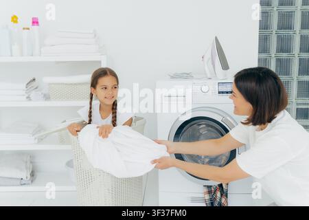 Mutter und Tochter waschen gemeinsam in einem weißen Waschraum mit Waschmaschine Stockfoto