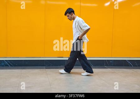 Junger Mann in lässiger Kleidung geht an einer lebhaften orangefarbenen Wand entlang. Urbane Mode und minimalistisches Ästhetik Stockfoto