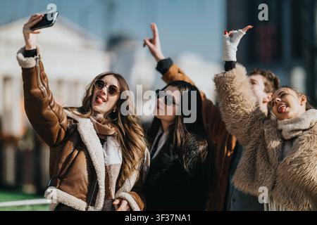Freunde machen ein lustiges Winter-Selfie zusammen an einer sonnigen Straße der Stadt mit Mänteln und Sonnenbrillen Stockfoto