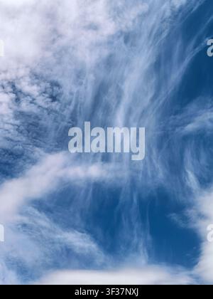 Zarte, fedrige Zirruswolken, die sich über einen tiefblauen Sommerhimmel erstrecken. Atmosphärische Wolkenlandschaft mit eleganten Hochgebirgsformationen, die eine dramatische Stockfoto
