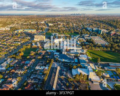Eine Luftperspektive des Campus der Deakin University und des vorstädtischen Wohngebiets mit der fernen Skyline von Melbourne unter warmem goldenem Ho Stockfoto
