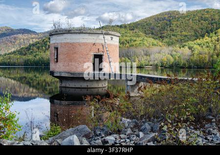 Alter Wasserentnahmeturm über einem Bergstausee in Primorje, Russland, umgeben von einer lebendigen Herbstwald und gespiegelt im ruhigen Wasser. Stockfoto