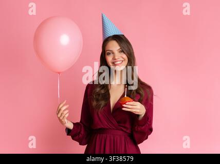 Glückliche junge Frau hält Cupcake und Ballon, Konzept für Geburtstagsfeier Stockfoto