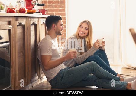 Glückliches junges Paar genießt zusammen Kaffee zu Hause, lächelt in gemütlicher Küche Stockfoto