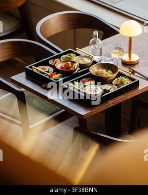 Hochwinkelschuss eines hölzernen Esstisches in einem Restaurant mit zwei kompletten japanischen Bento-Box-Sets, die auf schwarzen Tabletts serviert werden und Sushi enthalten. Stockfoto