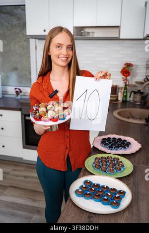 Frau lächelt und hat Nummer 10, die frisch gebackene Süßigkeiten in der Küche bekommt Stockfoto