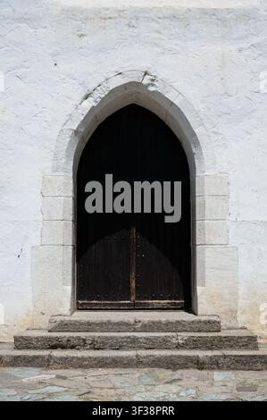 Dunkle mittelalterliche spitzbogige gotische Holztür mit Steinstufen an einer weiß getünchten Kirchenfassade in Szentendre, Ungarn. Stockfoto