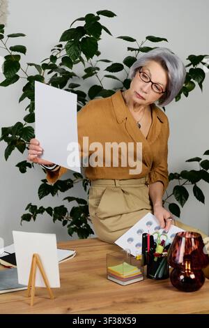Seniorin arbeitet fleißig in ihrem gemütlichen Heimbüro und prüft wichtige Dokumente Stockfoto