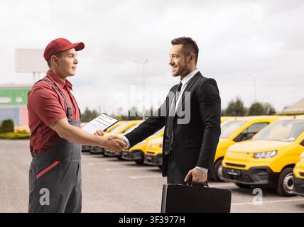 Geschäftsmann schüttelt einem Lieferkurier vor Gewerbetransportern die Hand Stockfoto