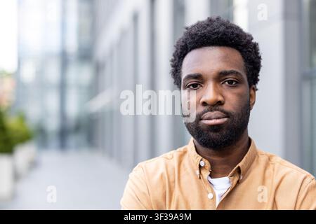 Selbstbewusster junger Mann mit Afro-Frisur und Bart steht im Freien vor einem modernen Bürogebäude und spiegelt Professionalität und Entschlossenheit in seiner Geschäftsumgebung wider Stockfoto