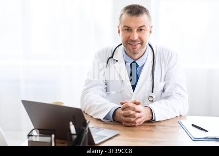 Porträt von reifen Arzt Blick auf Kamera sitzen am Schreibtisch Stockfoto