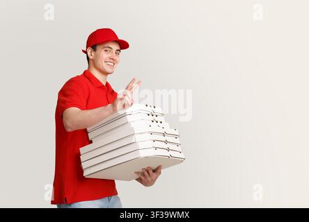 Eine Menge Pizza nach Hause. Lächelnder Kurier zeigt Friedenszeichen und hält viele Kisten Stockfoto