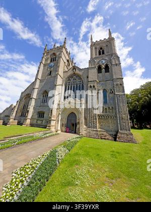 Einzigartige sommerliche Sicht von unten auf das King's Lynn Minster, das seine beiden Westtürme, ein großes Maßwerkfenster und eine mittelalterliche Steinfassade zeigt. Stockfoto