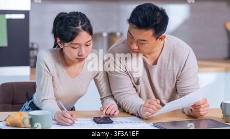Konzentrierte asiatische Frau und Mann arbeiten gemeinsam an Finanzen am Küchentisch, Geschäftskonzept Stockfoto