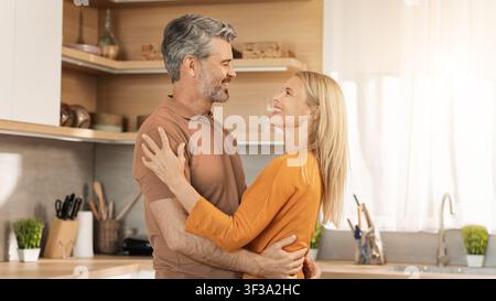 Glückliches Älteres Kaukasisches Paar, Das Sich In Der Küche Umschließt Und Eine Gute Gemeinsame Zeit Genießt Stockfoto