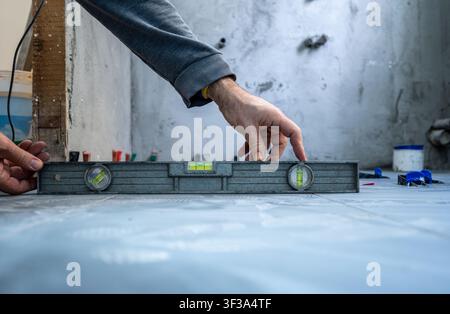 Arbeiter ebnet sorgfältig neu verlegte Fliesen auf einem Badezimmerboden während der Hausrenovierung und stellt sicher, dass der Installationsprozess perfekt und präzise verläuft Stockfoto