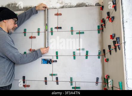 Erfahrener Bauarbeiter verwendet eine Wasserwaage, um die richtige Ausrichtung und Ebenheit bei der Installation neuer Keramikfliesen während eines Badezimmers oder Ki zu gewährleisten Stockfoto