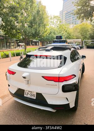 DALLAS, TX, USA - 13. JULI 2026: Ein autonomes Waymo-Jaguar-Fahrzeug steht auf einer Stadtstraße in Dallas, umgeben von Hochhäusern und Grünflächen Stockfoto
