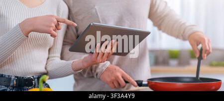Paar kocht zusammen in der Küche, nutzt Tablet für Rezept, konzentriert und engagiert Stockfoto