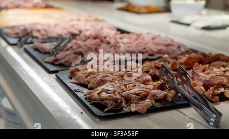 Verschiedene geschnittene Schinken, Prosciutto und gepfefferte Fleischsorten, die auf Tabletts an einem Hotel-Frühstücksbuffet serviert werden. Frische Cold Cuts zum Selbstbedienen in einem Restaurant. Stockfoto