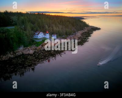 Bei der ersten Röte der Morgendämmerung steht der Bass Harbor Head Lighthouse als standhafter Wächter auf seinem felsigen Aussichtspunkt, eingebettet zwischen windgepeitschten Kiefern. Unten, th Stockfoto