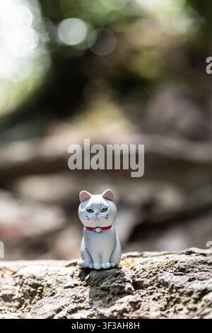 Chiang Mai, Thailand - 13. Juli 2026: Mürrisch aussehende weiße Katzenfigur mit einer roten Ameise in der Nähe, die auf einer Baumwurzel im Wald sitzt Stockfoto