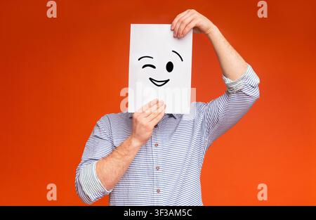 Junger Typ, der sein Gesicht unter einem gemalten zwinkernden Lächeln versteckt Stockfoto