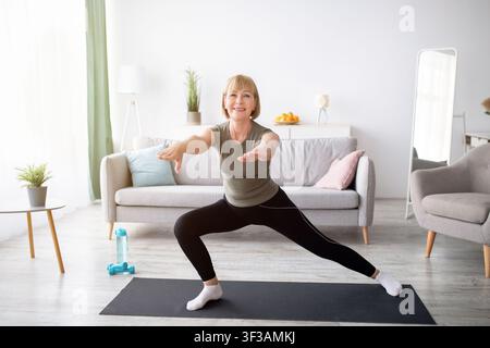 Glückliche ältere Dame, die Ausfallschritte beim häuslichen Training im Wohnzimmer macht, Platz kopieren Stockfoto