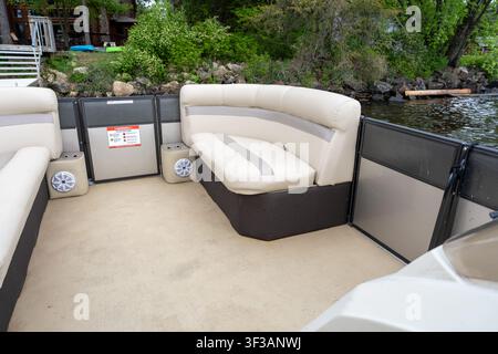 Eine weitläufige Innenaufnahme eines Pontonboots, die bequeme beige und braune gepolsterte Loungesitze, einen Teppichboden, eingebaute Lautsprecher und einen Blick auf die Stockfoto