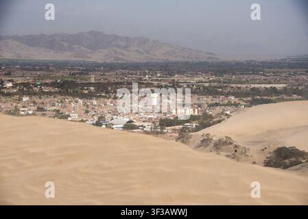 Ein Luftpanorama fängt eine lebendige Stadt mitten in weiten Wüstendünen und fernen Bergen ein Stockfoto