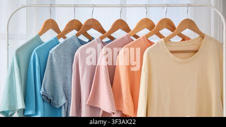 Pastellfarbene T-Shirts, die an Holzbügeln hängen Stockfoto