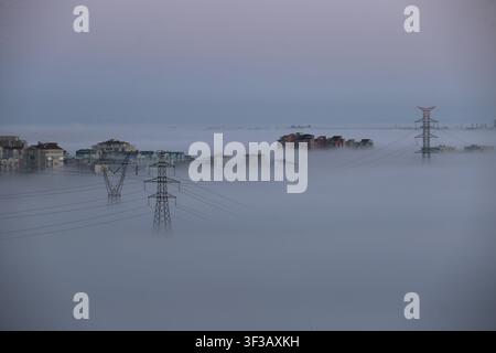 Elektrische Übertragungsmast mit Stadtgebäuden bei nebligem Sonnenaufgang in Istanbul, Türkei. Stockfoto