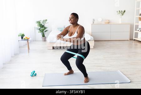 Mollige tausendjährige schwarze Frau, die während des häuslichen Trainings mit Gummiband hockt, freier Platz Stockfoto