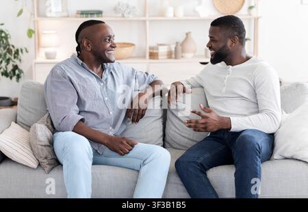 Erwachsener Sohn Und Älterer Vater Sprechen Während Der Entspannung Auf Der Couch Zu Hause Stockfoto