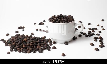 Weiße Tasse gefüllt mit gerösteten Kaffeebohnen und verstreuten Bohnen Stockfoto